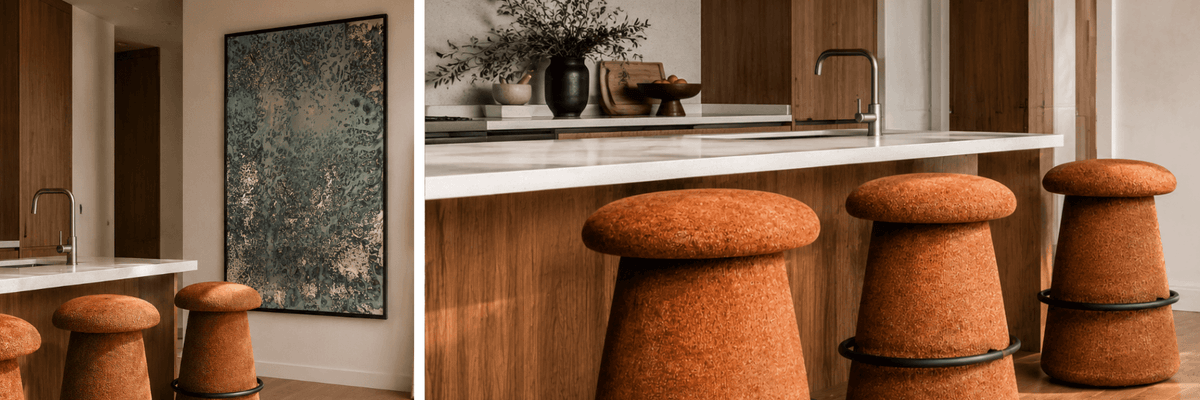 A split-view interior scene showing a kitchen island with tall orange upholstered bar stools and a framed abstract artwork on the wall.