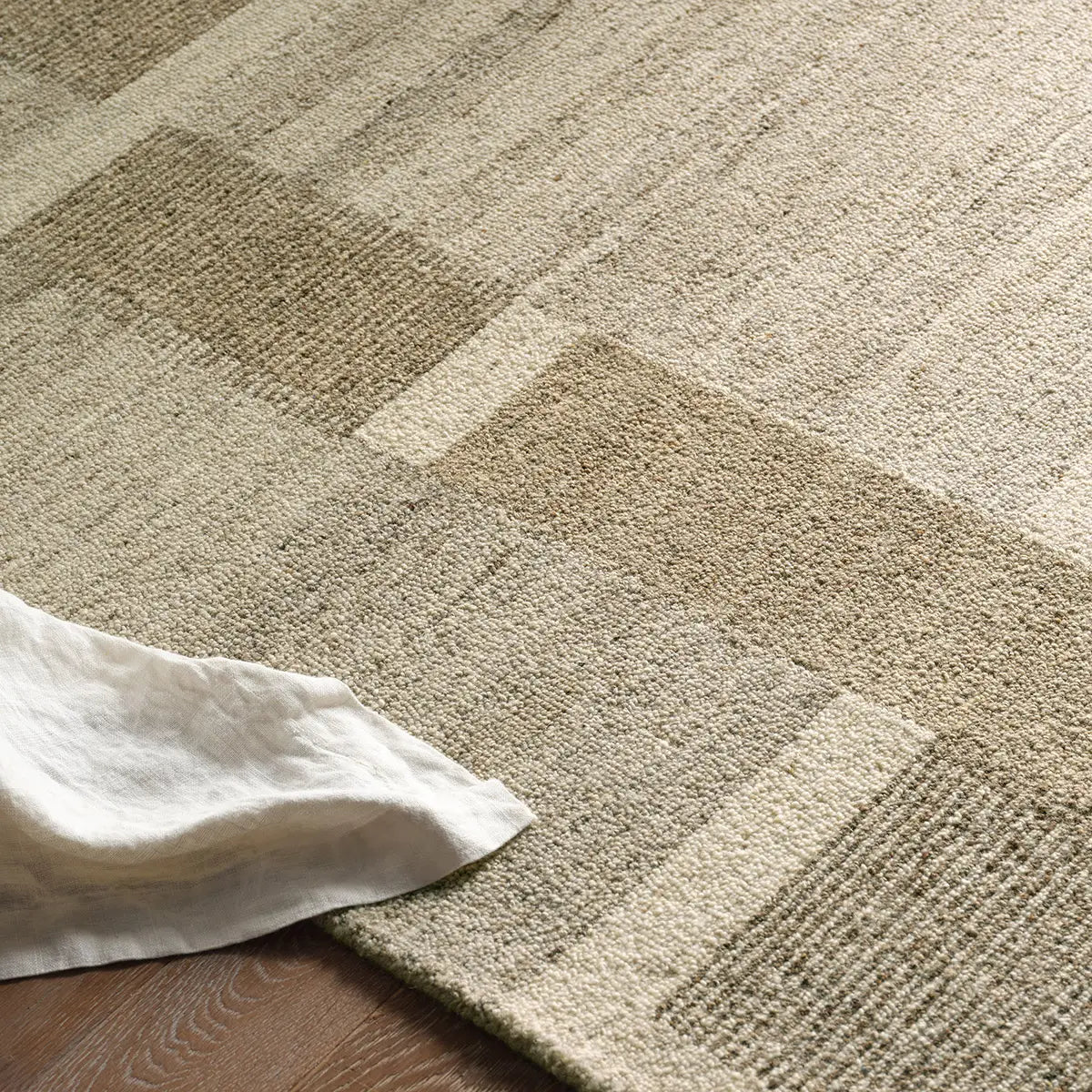 Close-up of a textured beige carpet with a white cloth on a wooden floor.