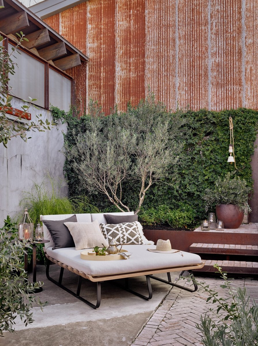 Outdoor patio with a sofa, cushions, and decorative items against a brick wall.