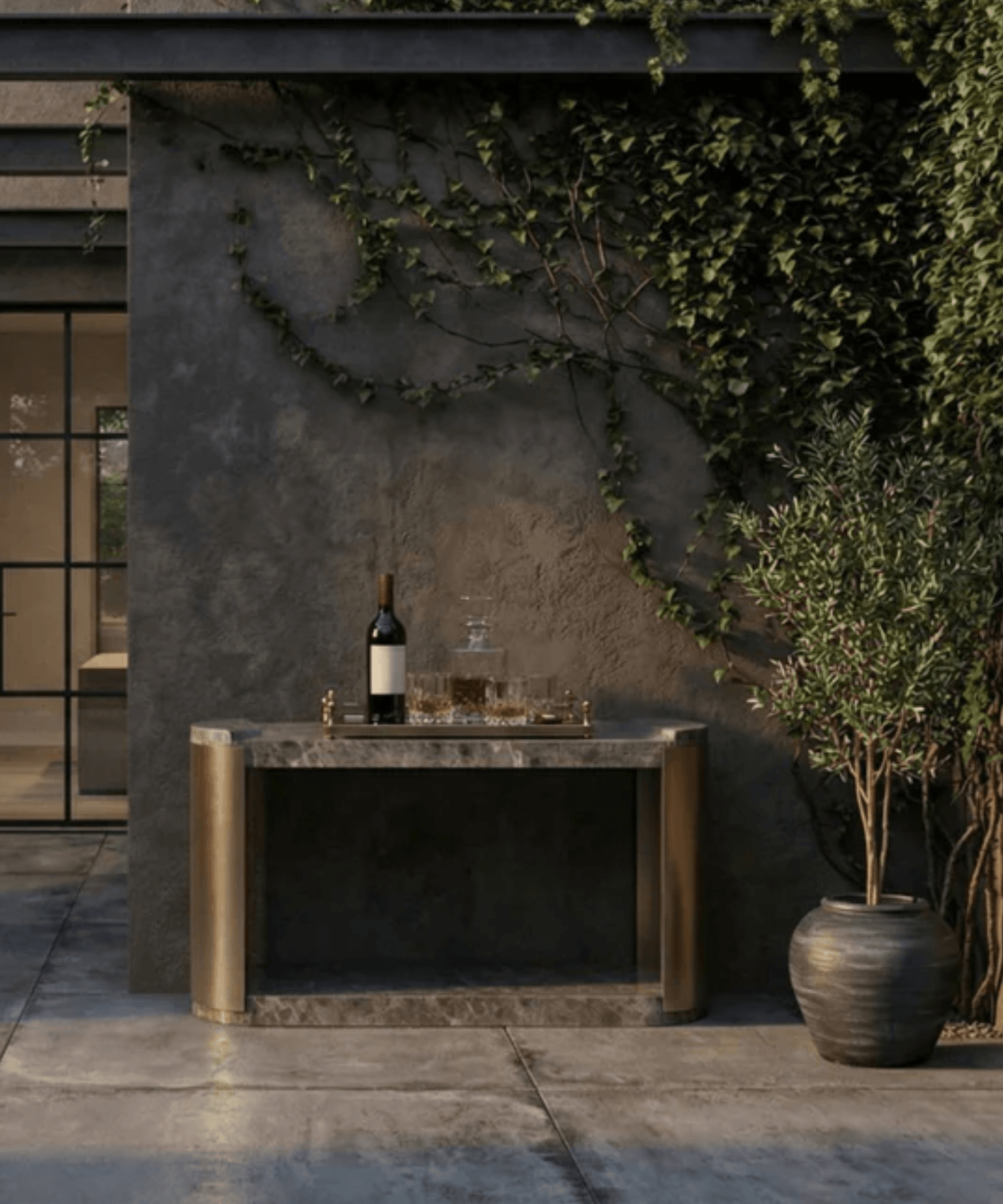 Outdoor setting with a stone table, wine bottle, and glasses against a textured wall with greenery.