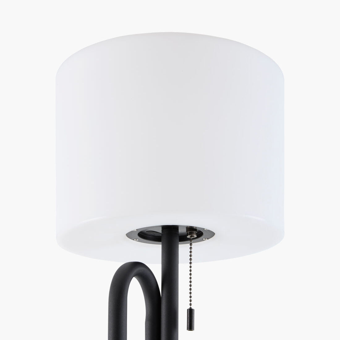 A close-up of a modern floor lamp featuring a large white cylindrical drum shade and a matte black metal frame with a pull chain.