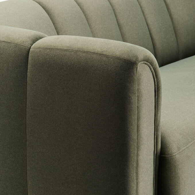 Close-up of a modern upholstered armchair or sofa in a muted sage green fabric, showing the rounded armrest, vertical channel tufting on the back, and clean seam lines.