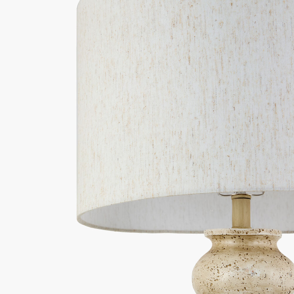 Close-up of a table lamp with a textured off-white fabric drum shade and a speckled beige ceramic base on a white background.