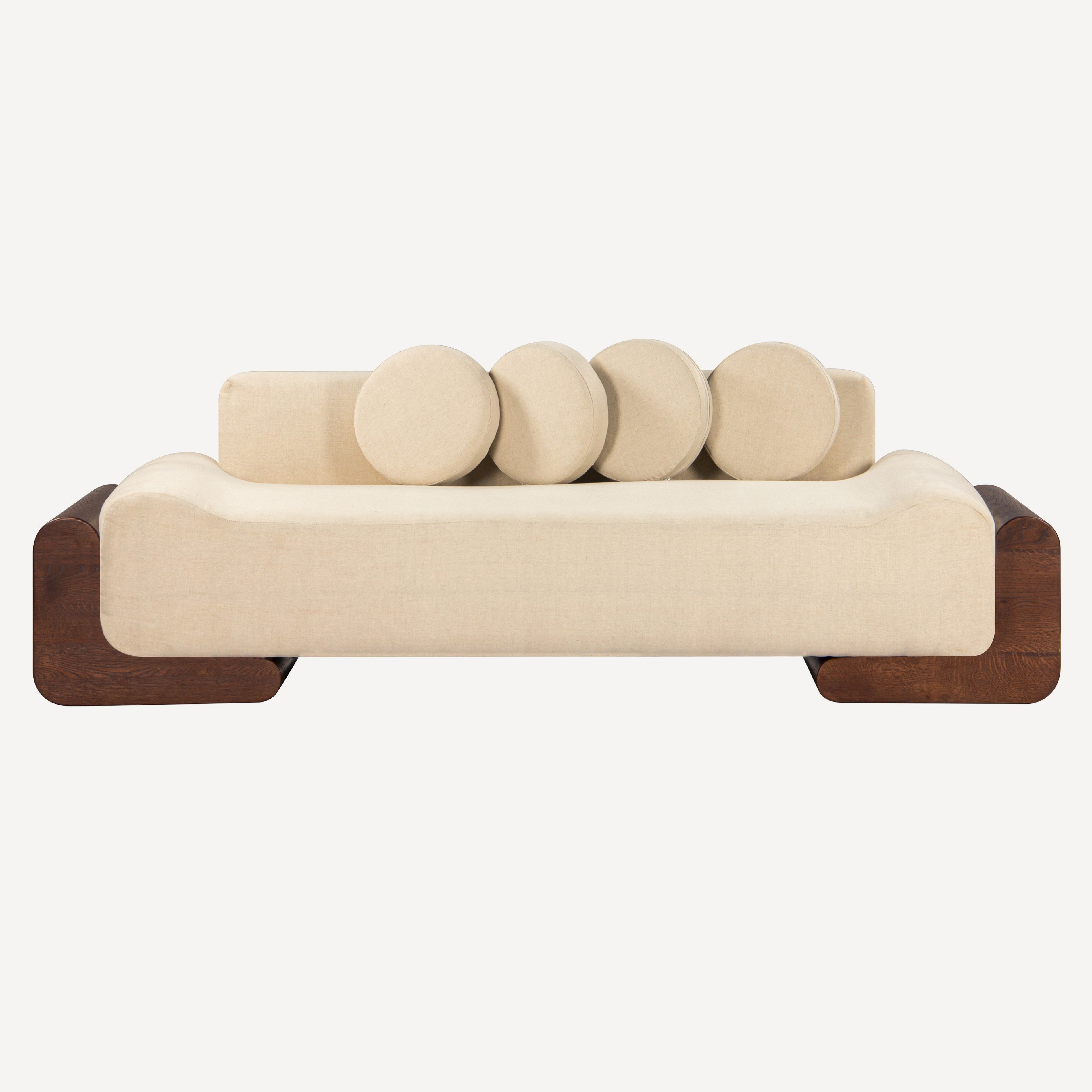 A modern low-profile daybed sofa with a cream-colored upholstered seat and backrest, featuring five round back cushions and dark brown wooden side supports, shown against a solid off-white background.
