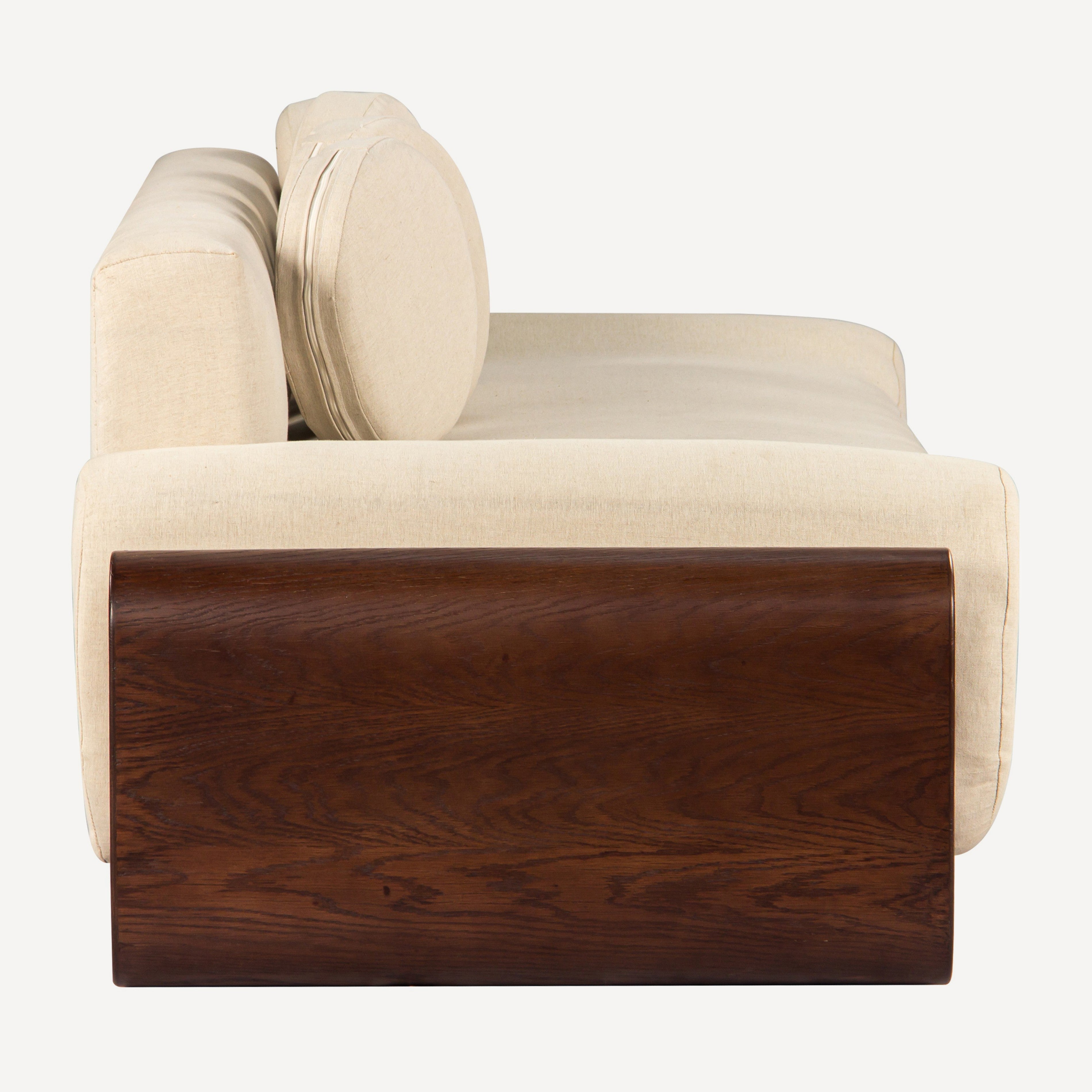 A modern low-profile sofa with cream-colored fabric upholstery and a prominent dark brown wood panel base, shown from a side angle against a plain white background.