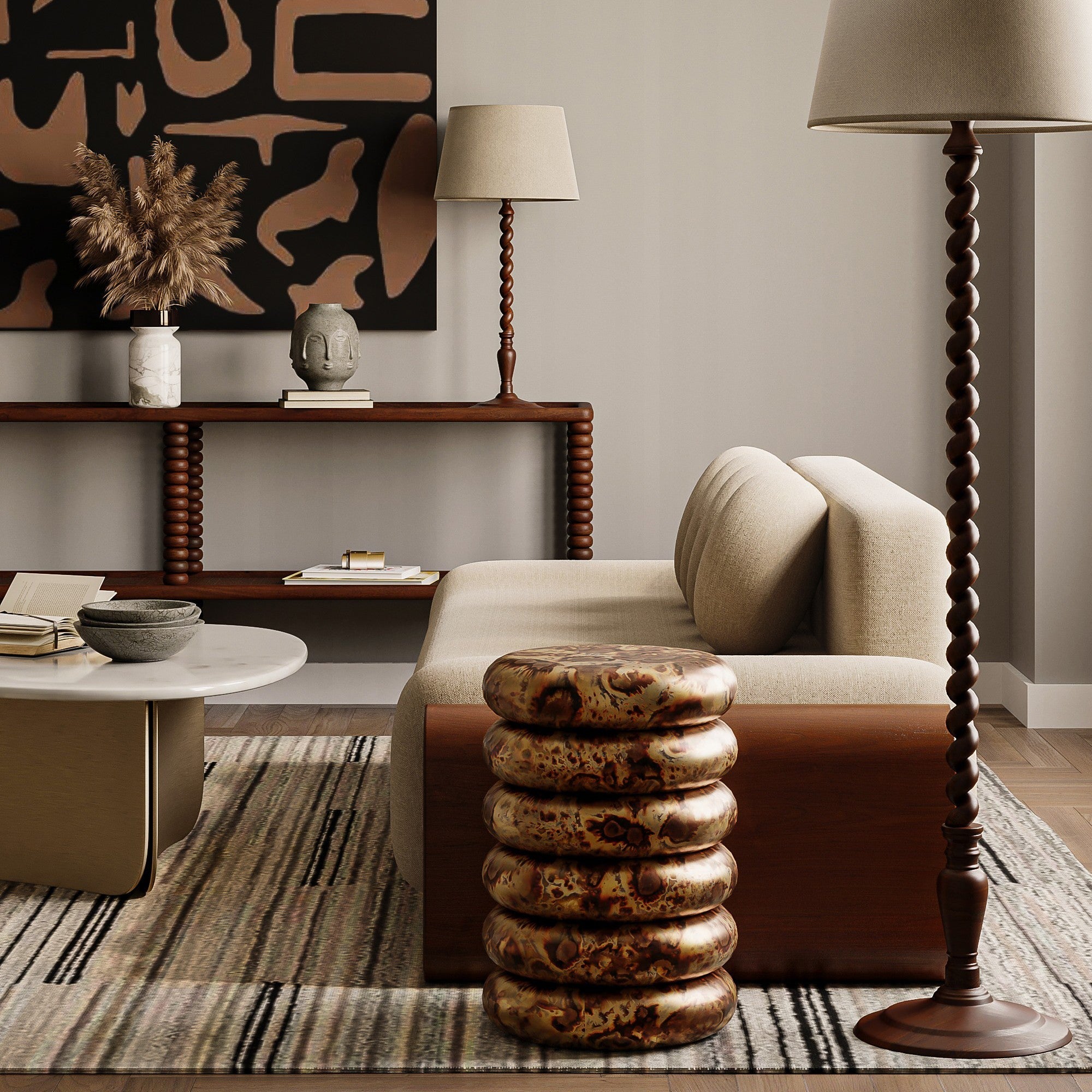 A styled living room scene featuring a cream upholstered sofa with a brown leather side panel, a stacked metallic gold side table in the foreground, a striped rug, a wooden console shelf with decor, and a tall floor lamp.