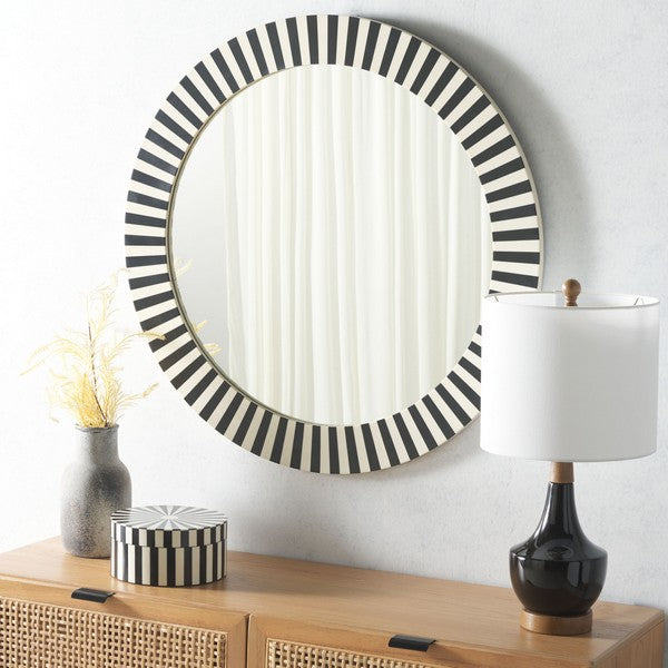 Round mirror with black and white striped frame on a wall above a wooden console table.