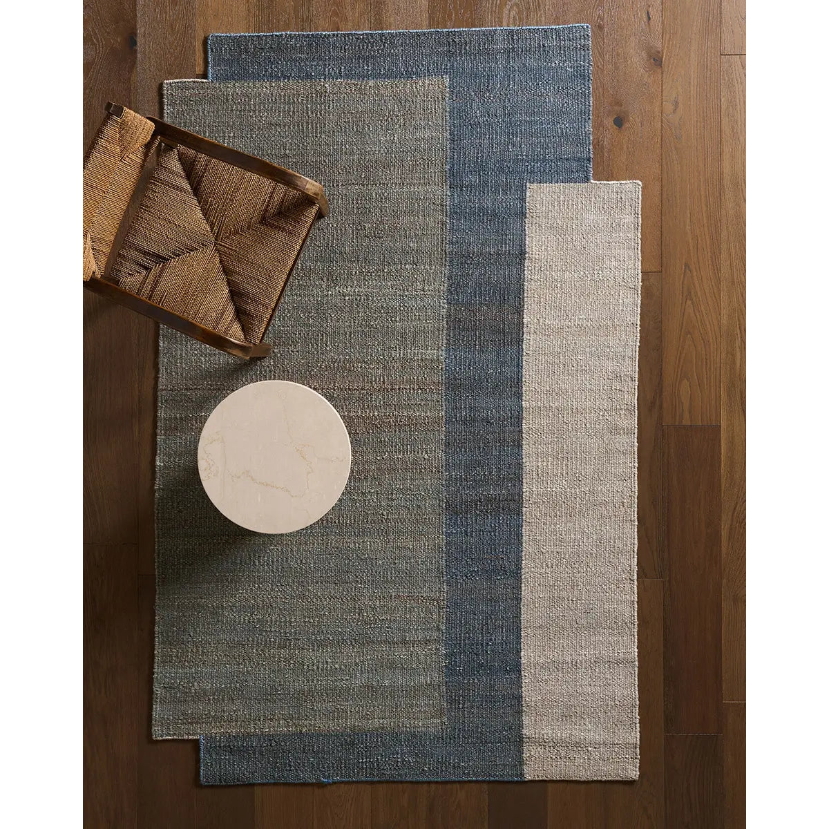 Asymmetrical blue and gray rug on a hardwood floor  with a woven accent chair and white marble side table 