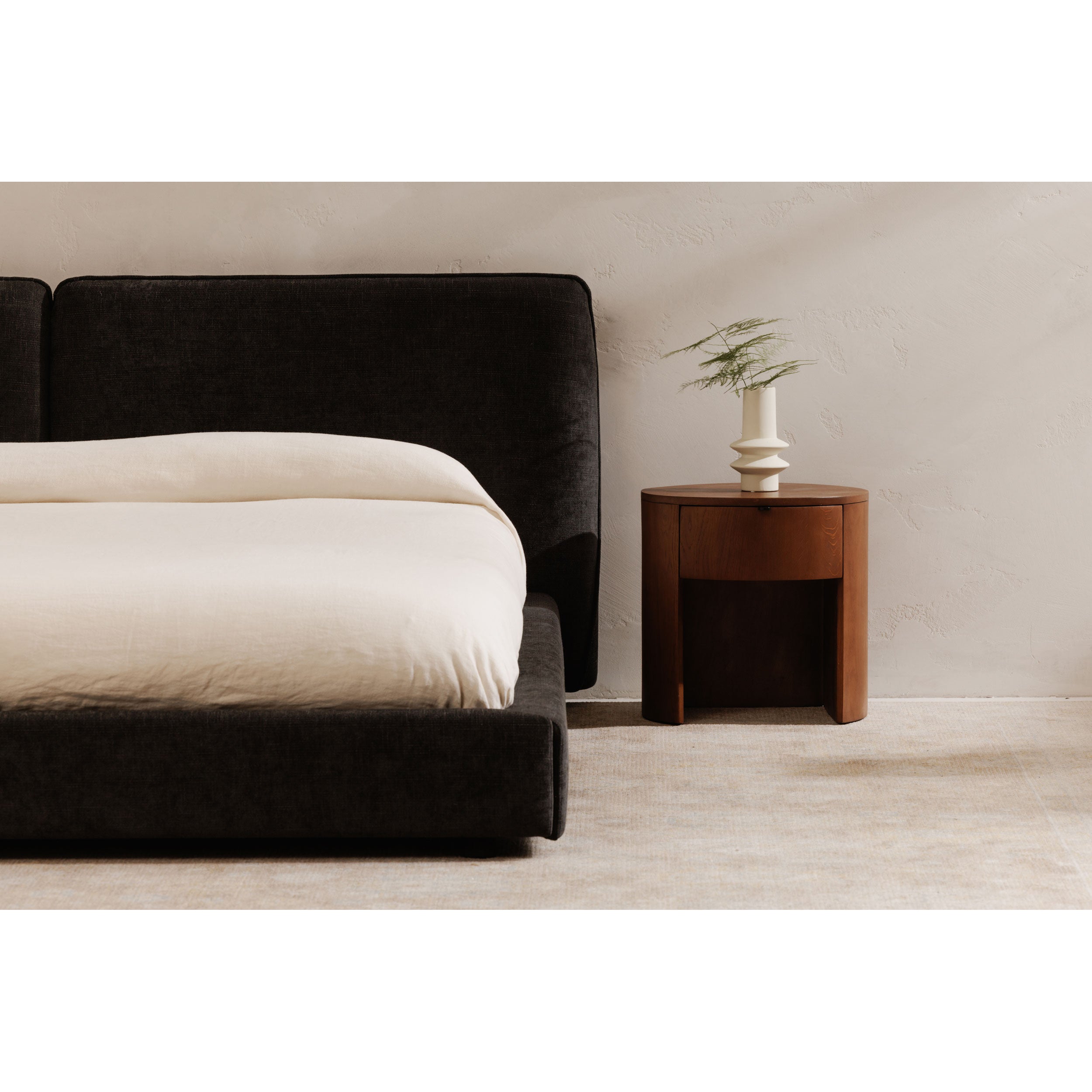 Modern bedroom with a black upholstered bed and round wooden nightstand.