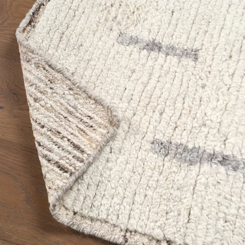 Close-up of a textured beige rug corner on a wooden floor