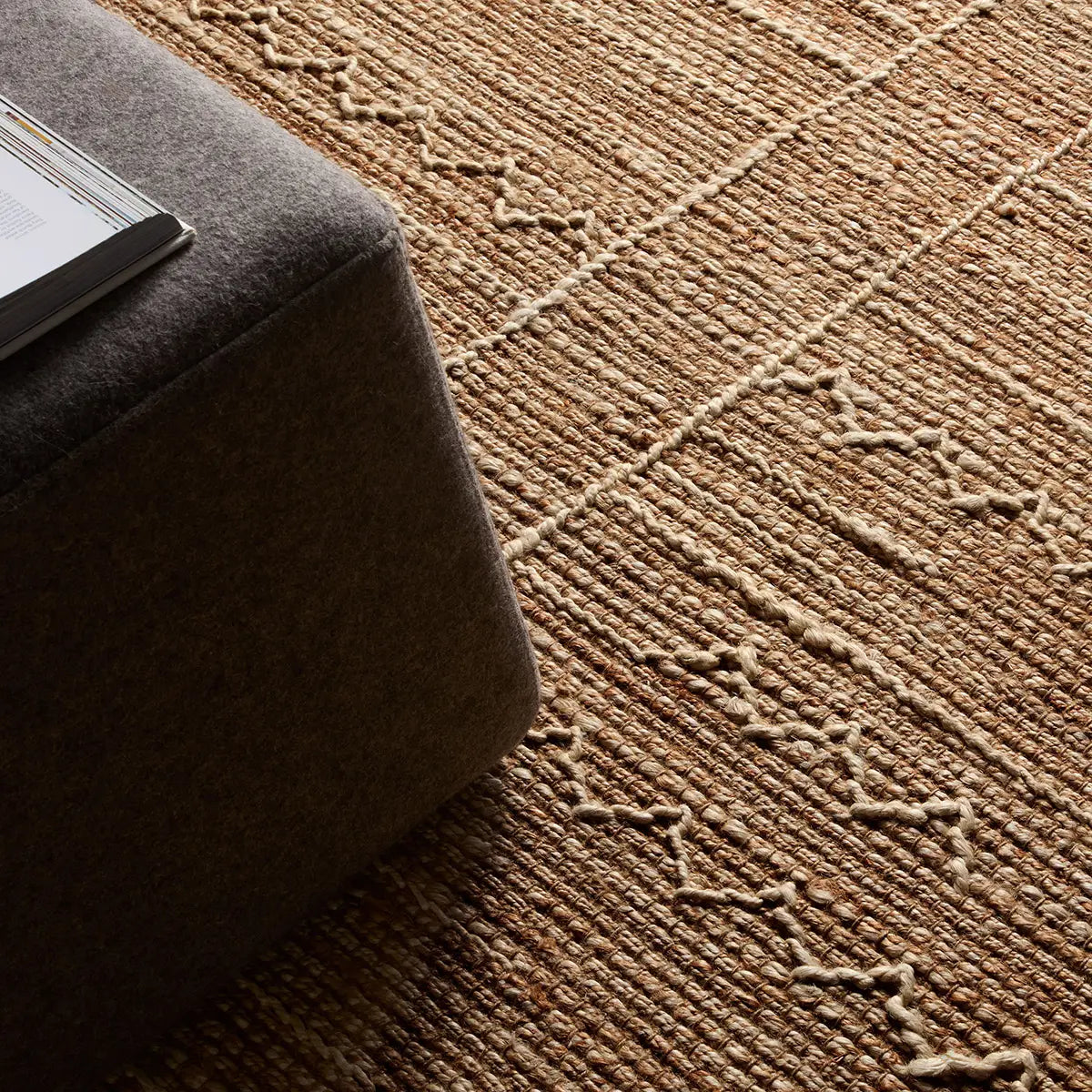 Brown textured rug with geometric pattern next to a dark brown ottoman.
