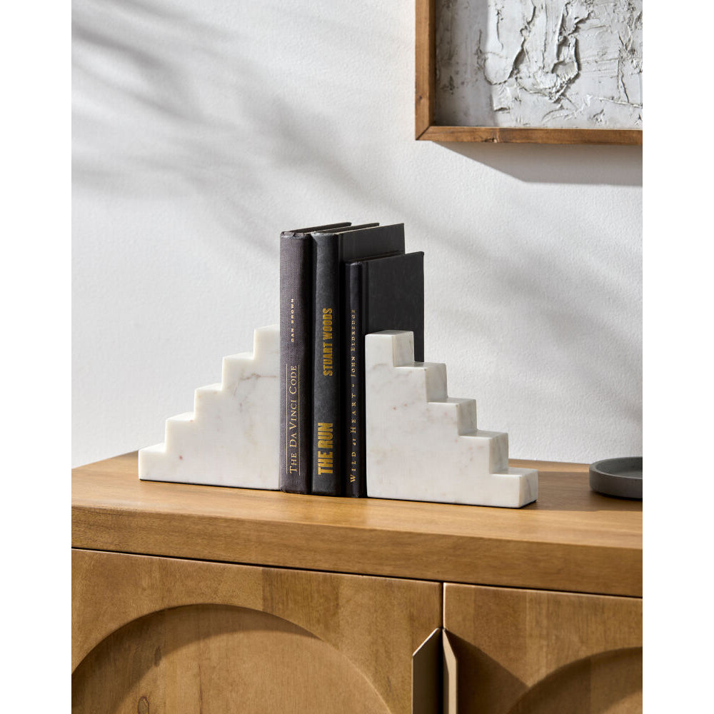 Decorative bookends on a wooden surface with books and a framed picture in the background.
