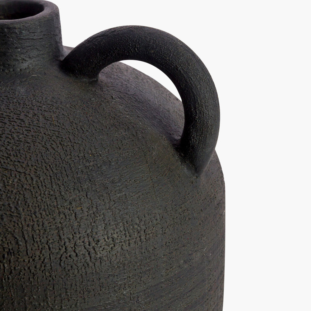 Black textured ceramic vase with a handle on a white background