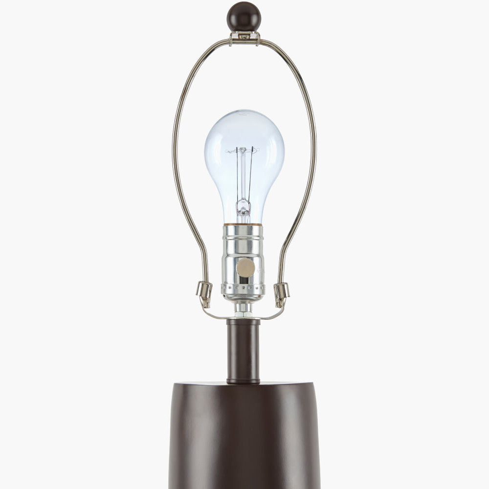 A close-up of a table lamp featuring a dark brown cylindrical base, a polished silver metal arched shade, and a clear glass bulb, shown against a plain light gray background.