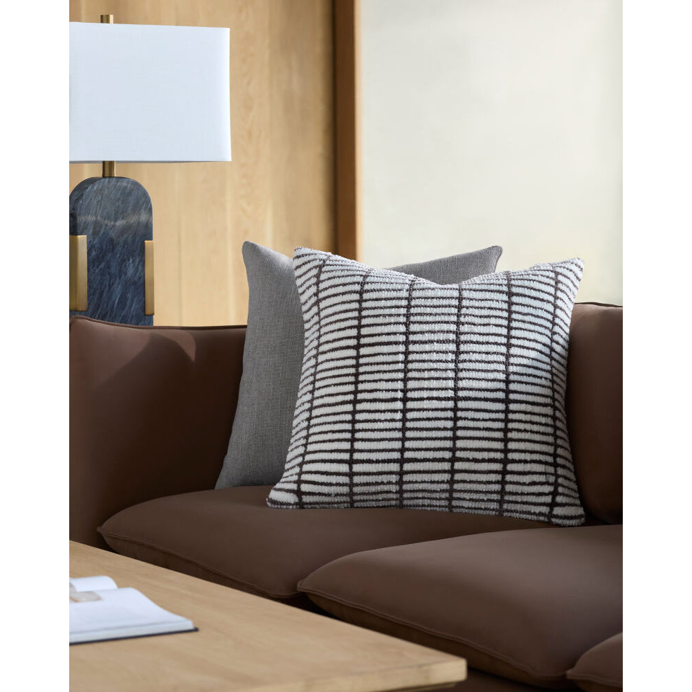 Decorative pillows on a brown sofa with a lamp and table in the background.
