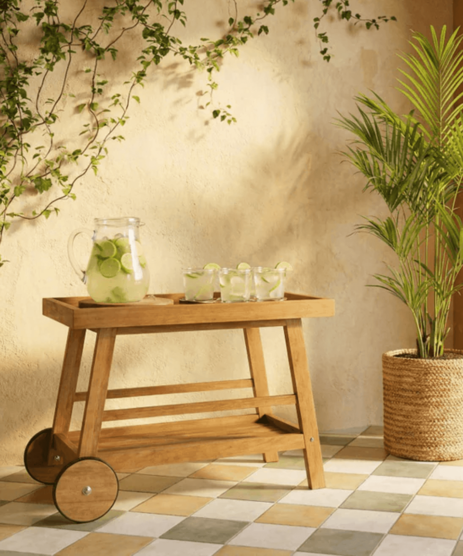 Wooden serving cart with drinks and a plant on a checkered floor.