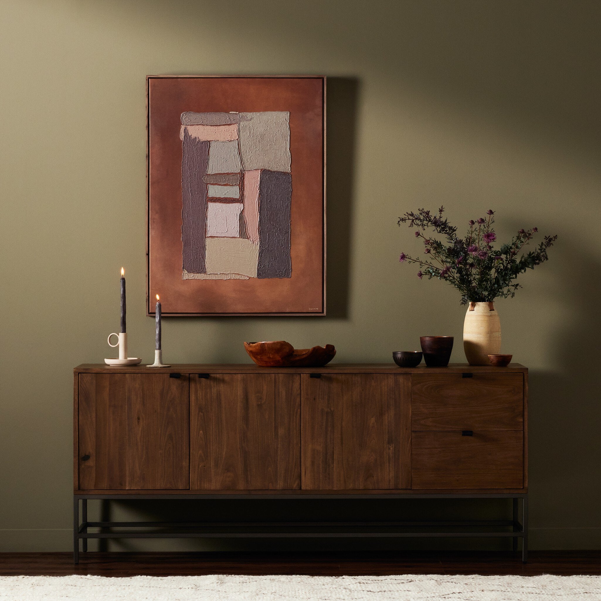 Solid wood sideboard with decorative items against a green wall with a framed abstract painting.