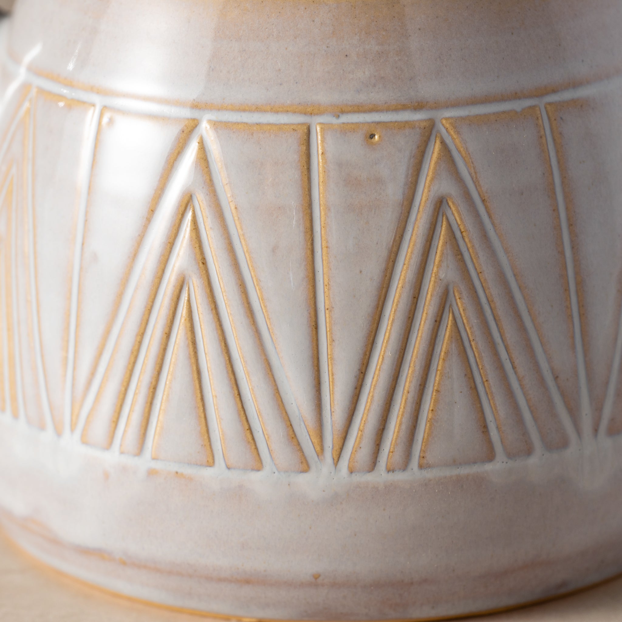 Close-up of a ceramic vase with geometric gold patterns on a beige background