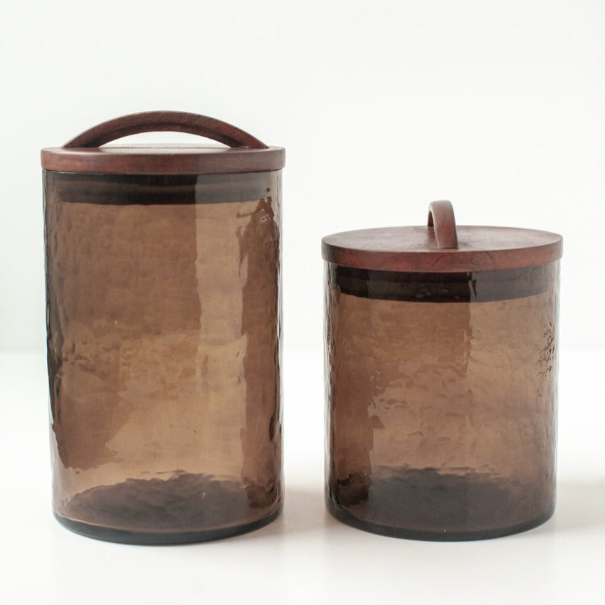 Two brown glass canisters with wooden lids on a white background