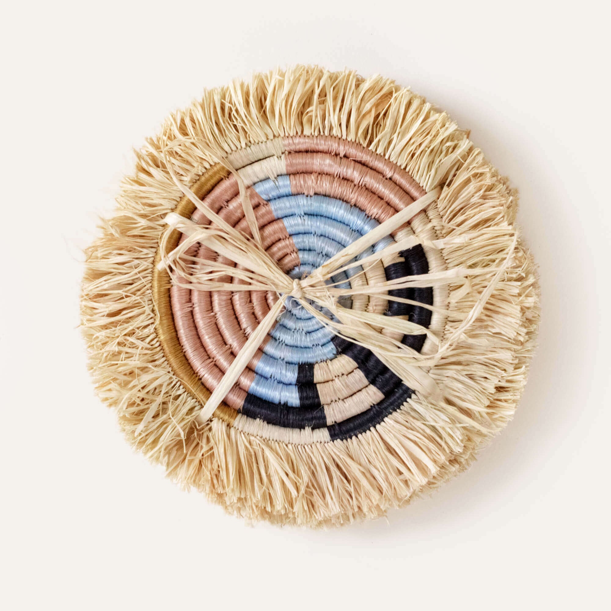 Round woven coaster with colorful concentric circle design on a white background