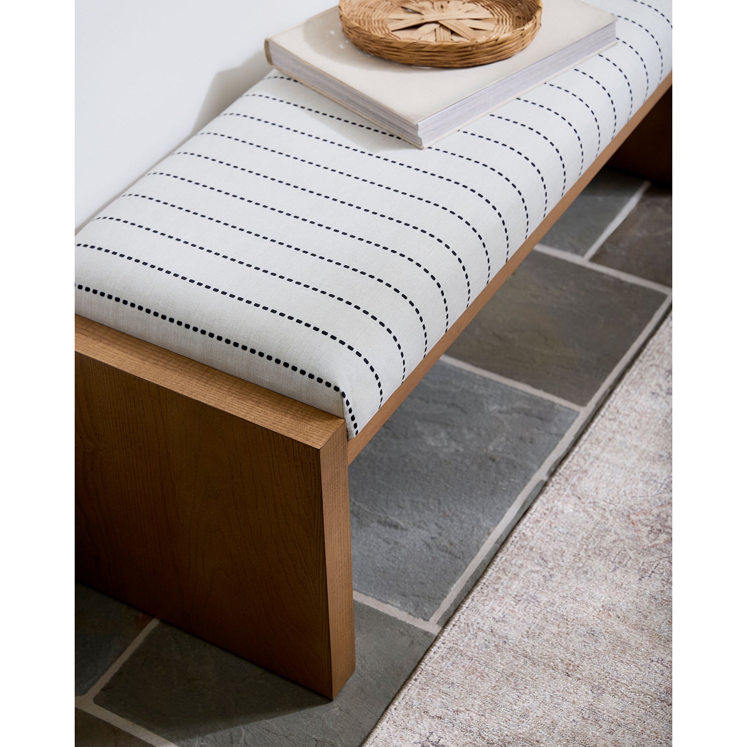 Wooden bench with a white cushion featuring black stitching on a stone floor.