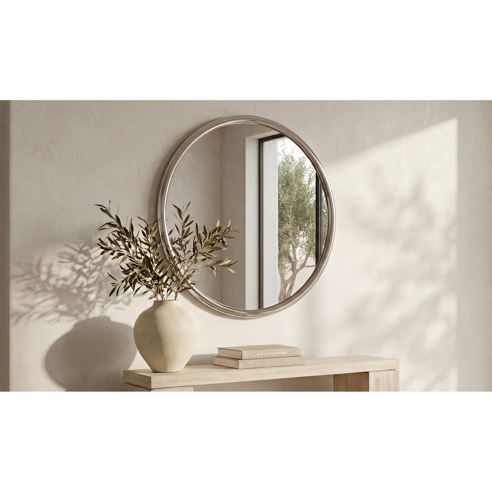 Round mirror on a wall with a vase and books on a table below.