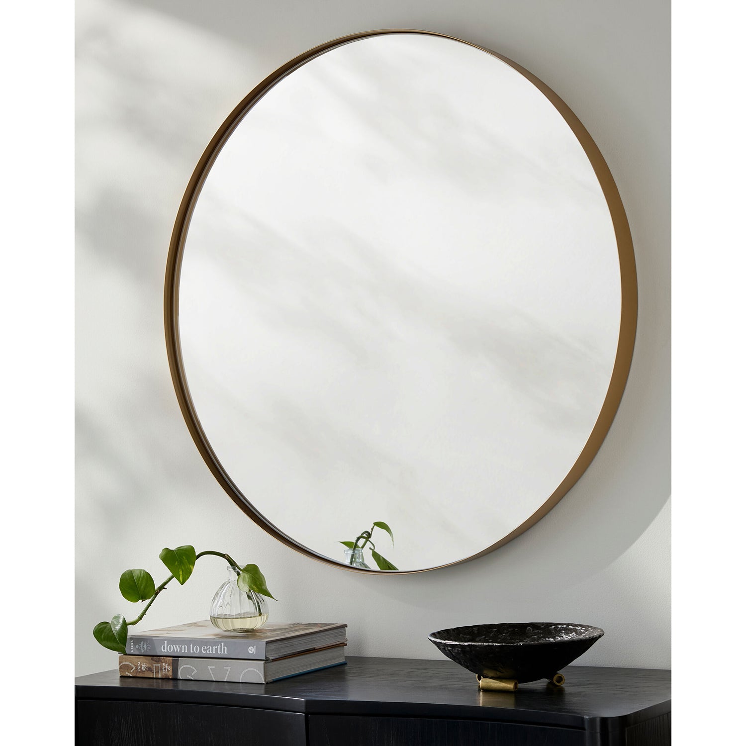 Round wall mirror with wooden frame on a neutral wall above a dark surface with decorative items.