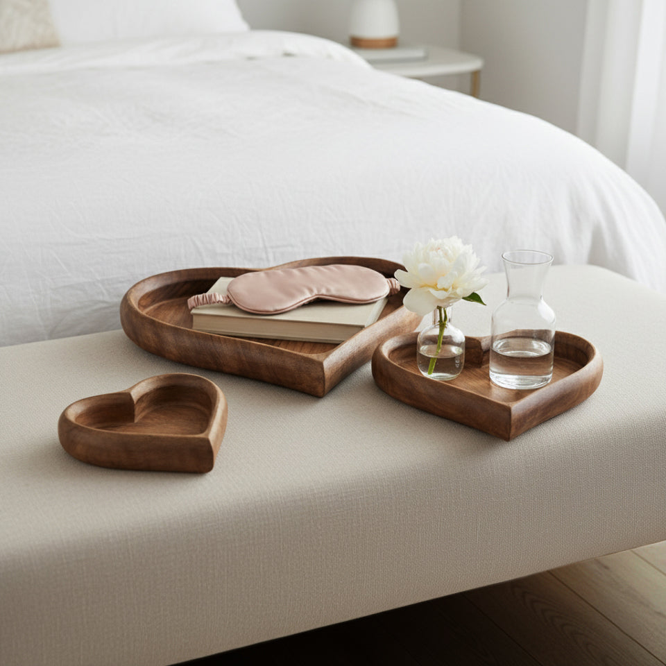 Wooden trays with a sleep mask, books, and a glass of water on a bed.