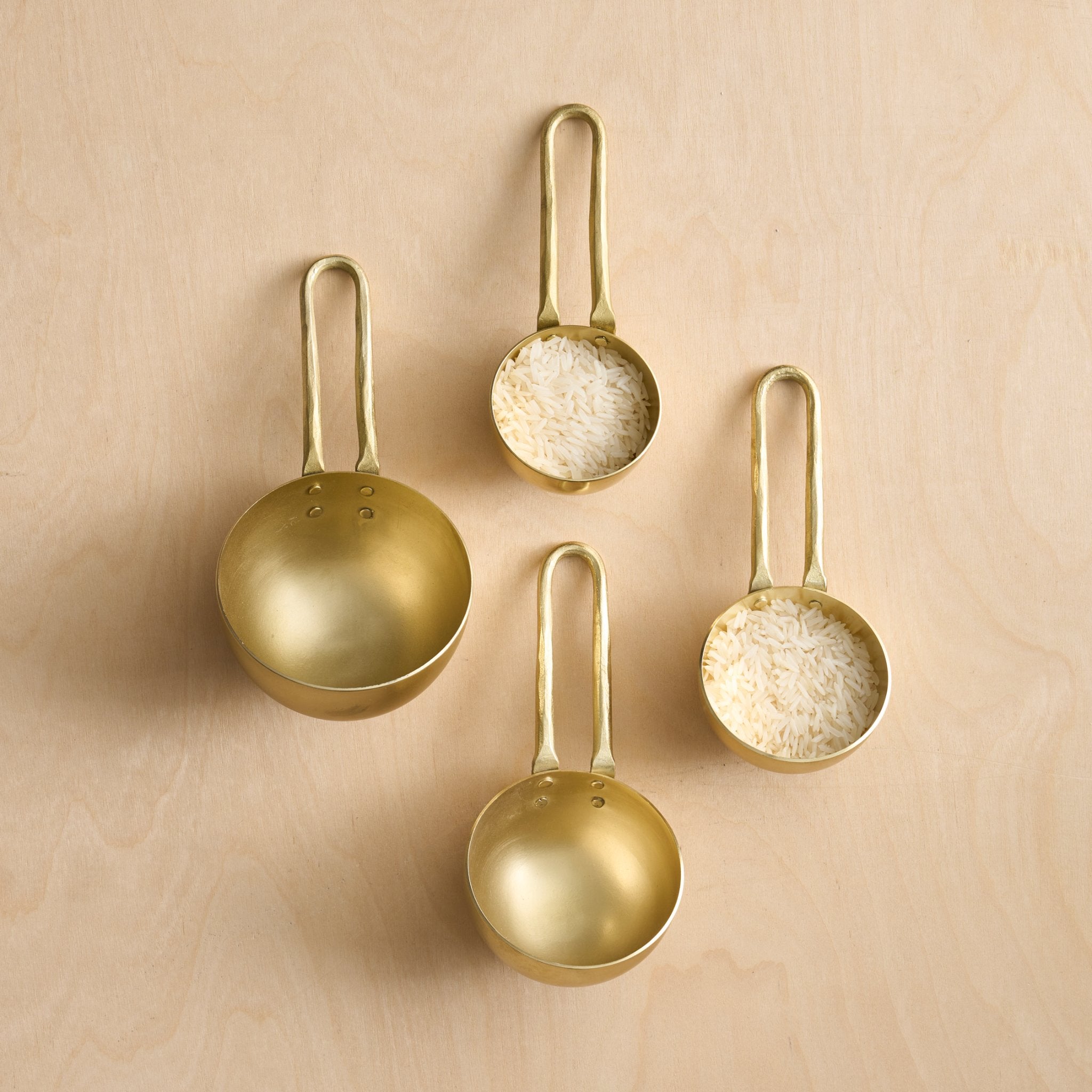 Set of four gold measuring spoons with different capacities on a beige background