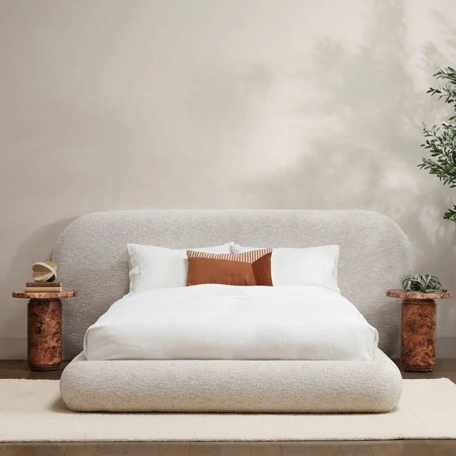 Neatly made bed with white bedding and brown accent pillow in a minimalistic room.