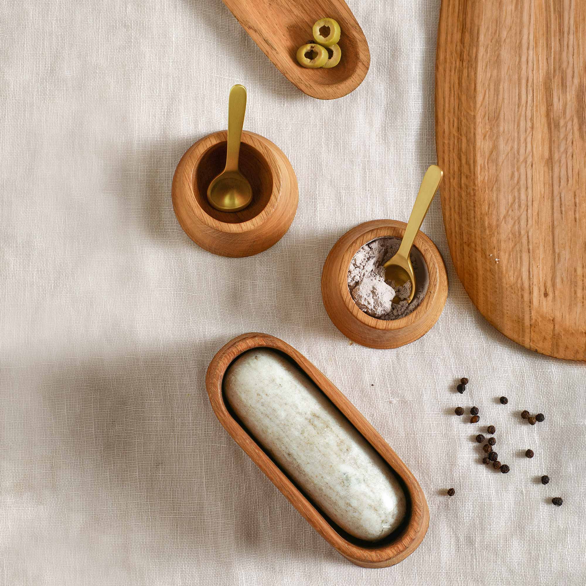 Wooden mortar with a marble pestle on a textured surface with small wooden bowls and spoons.