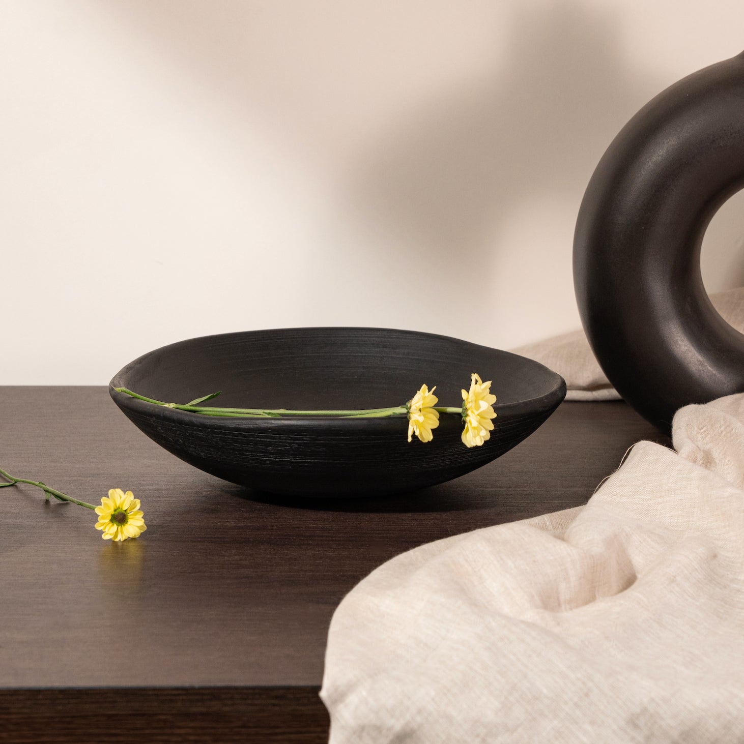 Black ceramic bowl with yellow flowers on a wooden surface, with a neutral background