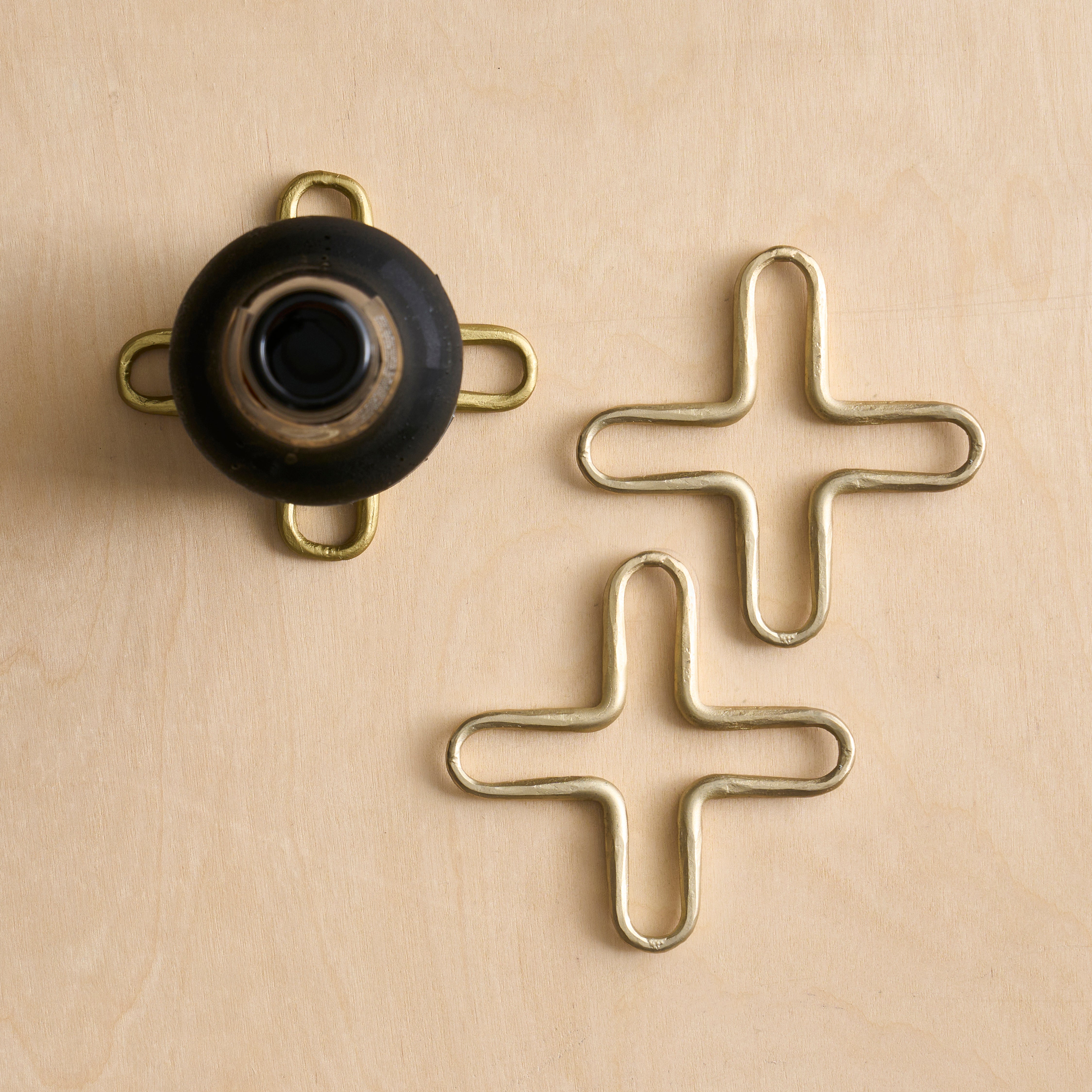 Brass cross-shaped trivets on a beige background
