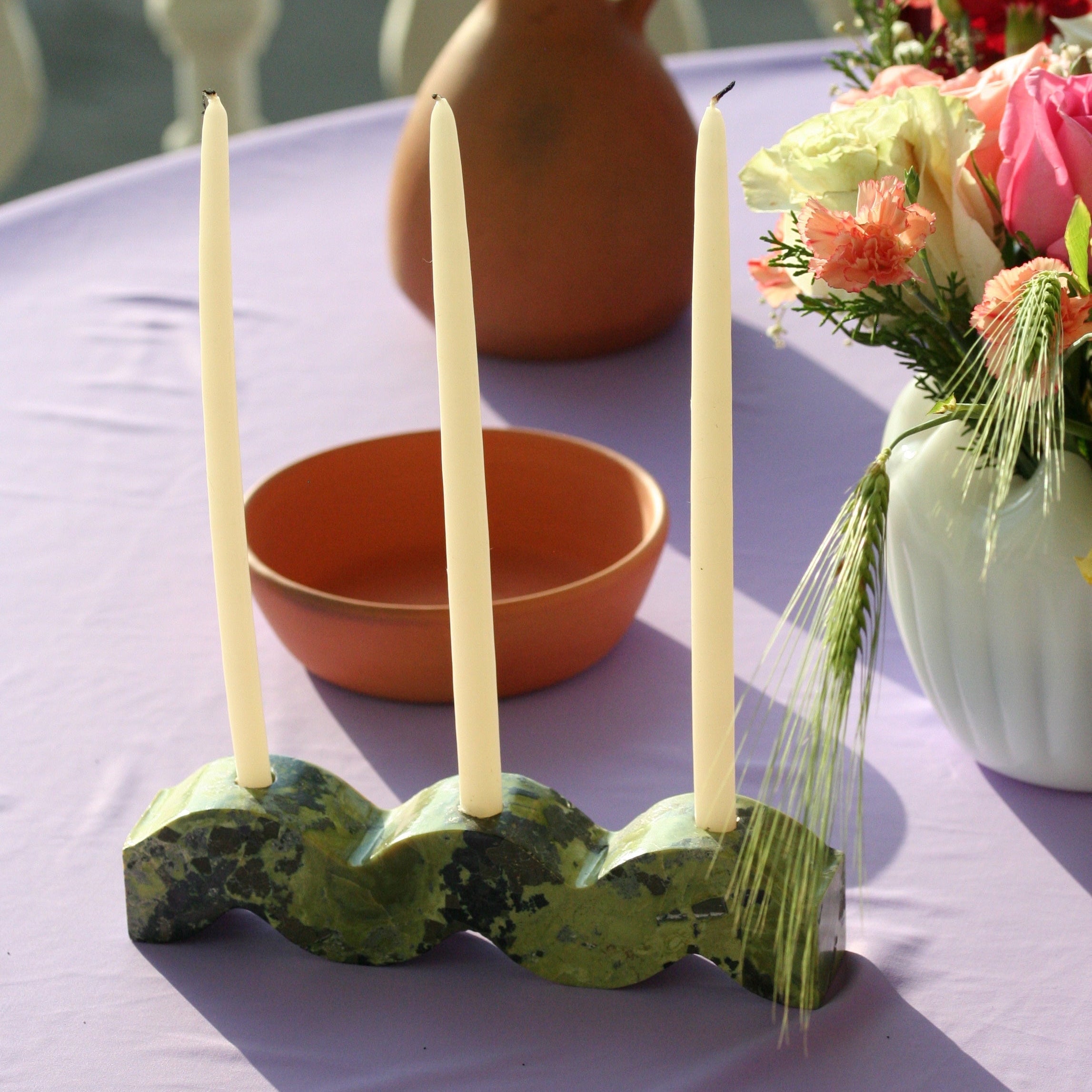 Decorative candle holder with candles on a table with a vase and flowers in the background.