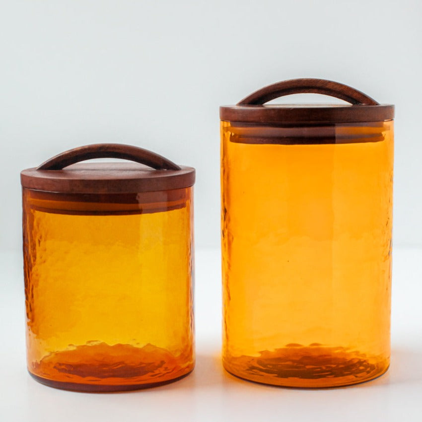Two orange glass canisters with wooden lids on a white background