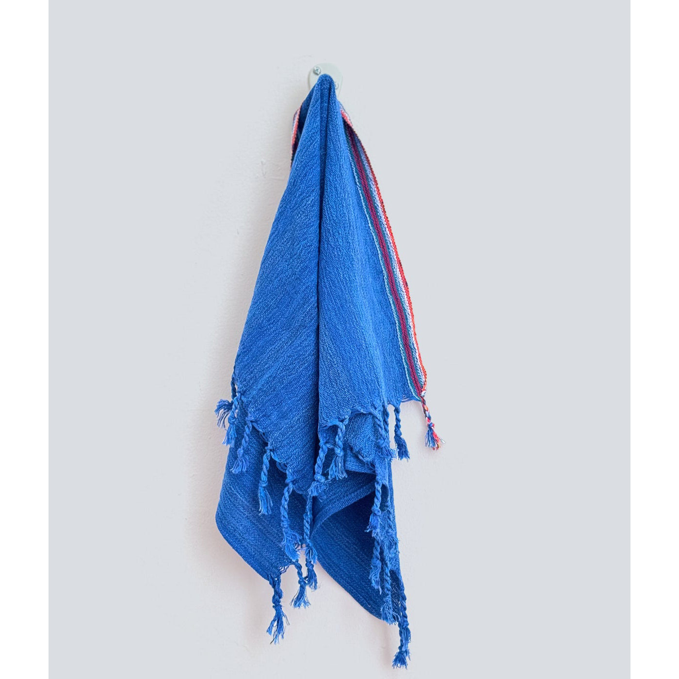 Blue hand towel with tassels hanging on a light gray background