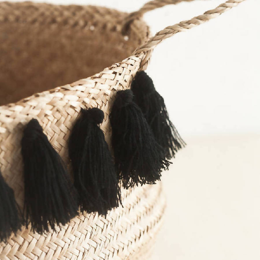Woven basket with black tassels on a neutral background
