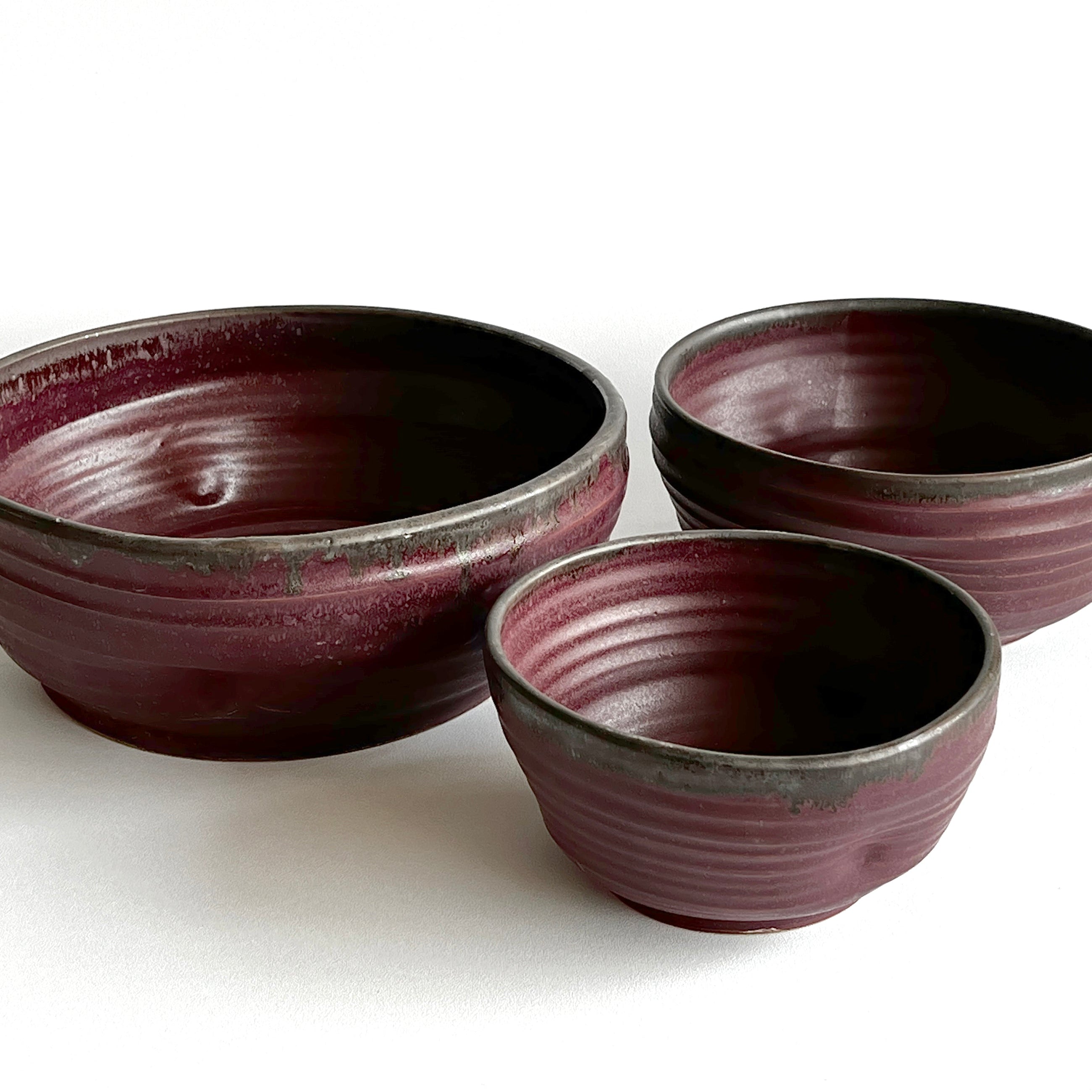 Three ceramic bowls with a maroon and black glaze on a white background