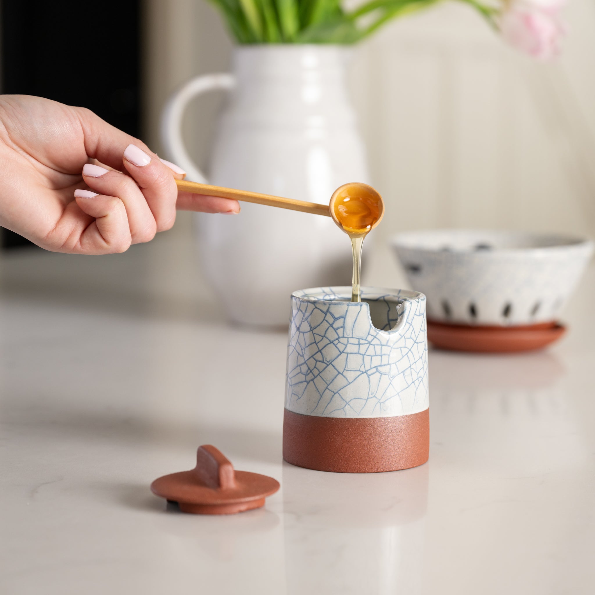Person pouring honey into a ceramic container with a cracked glaze design.