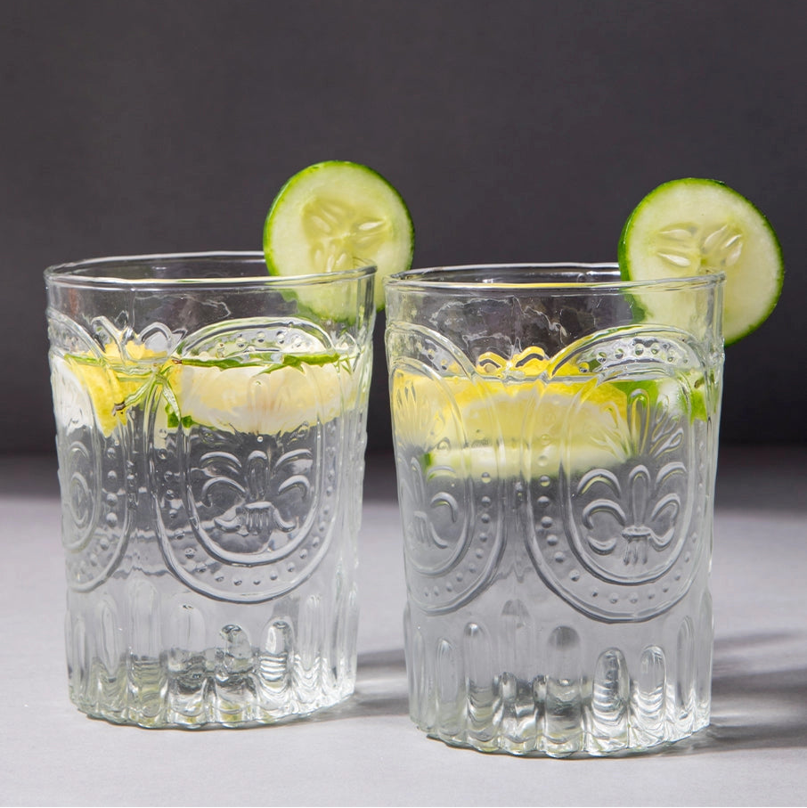 Two glass tumblers with lemon and cucumber slices on a dark background