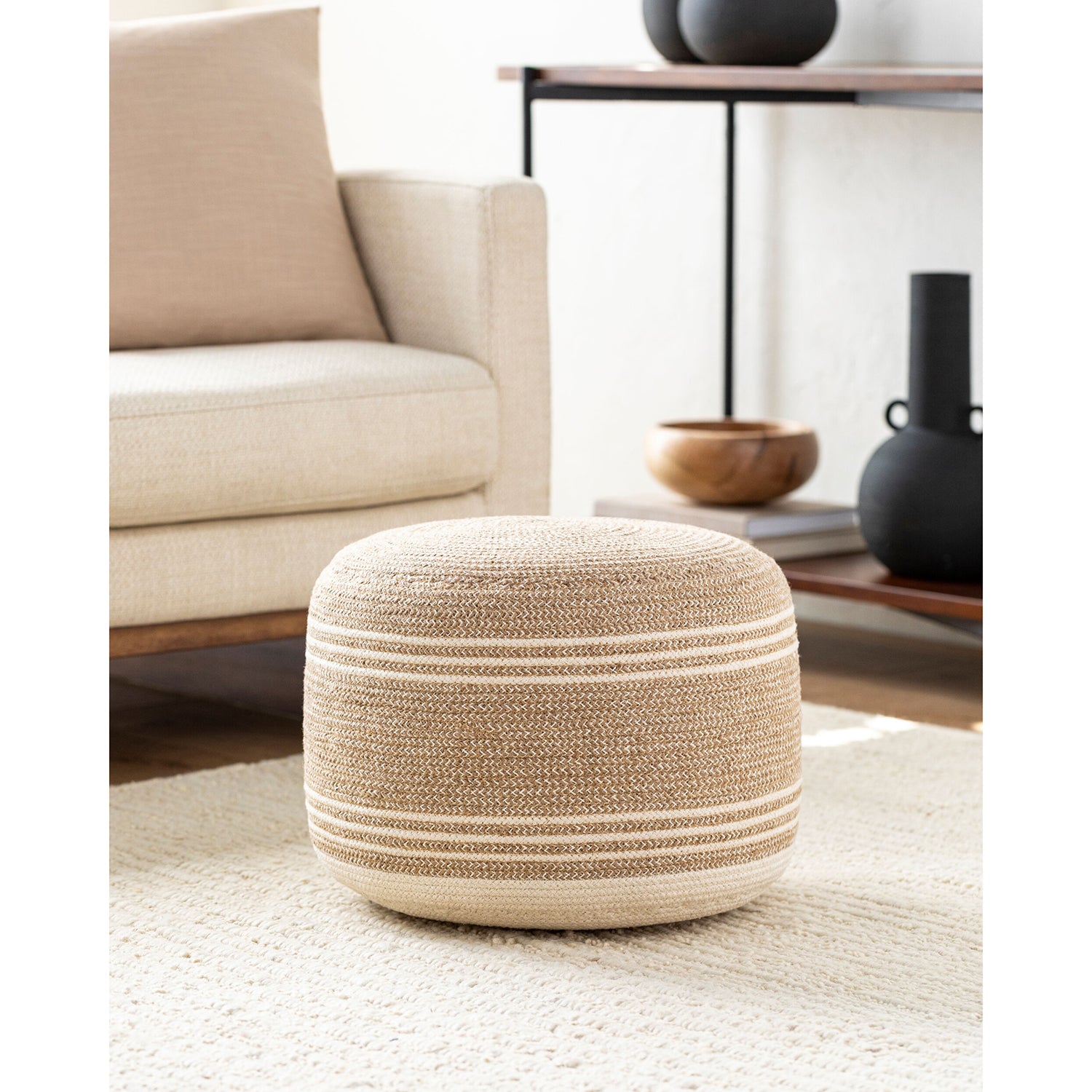 Beige woven ottoman in a living room setting with a beige sofa and wooden coffee table.