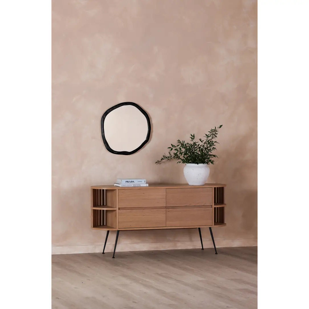 Wooden sideboard against a beige wall with a round mirror and plant on top