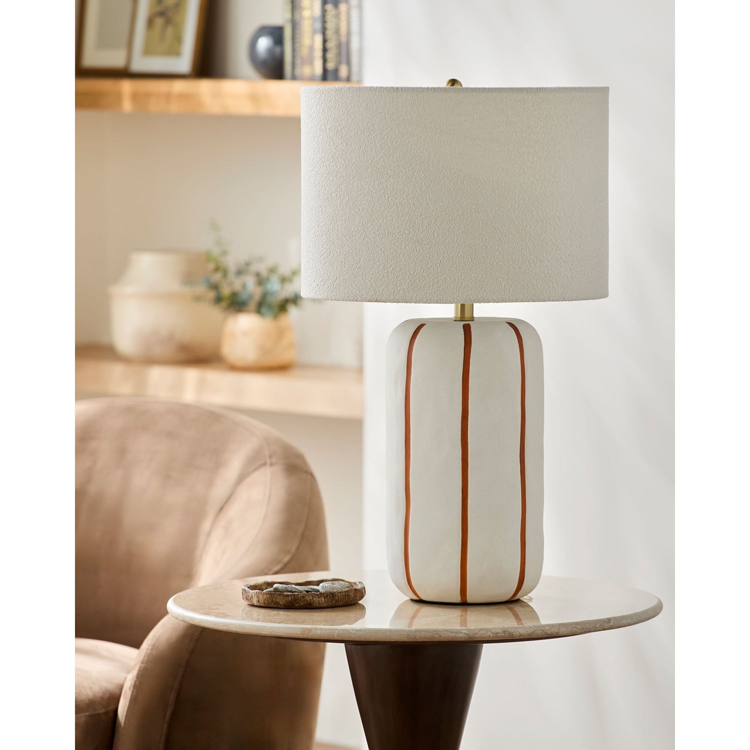 Table lamp with a beige base and white shade on a side table in a room setting.