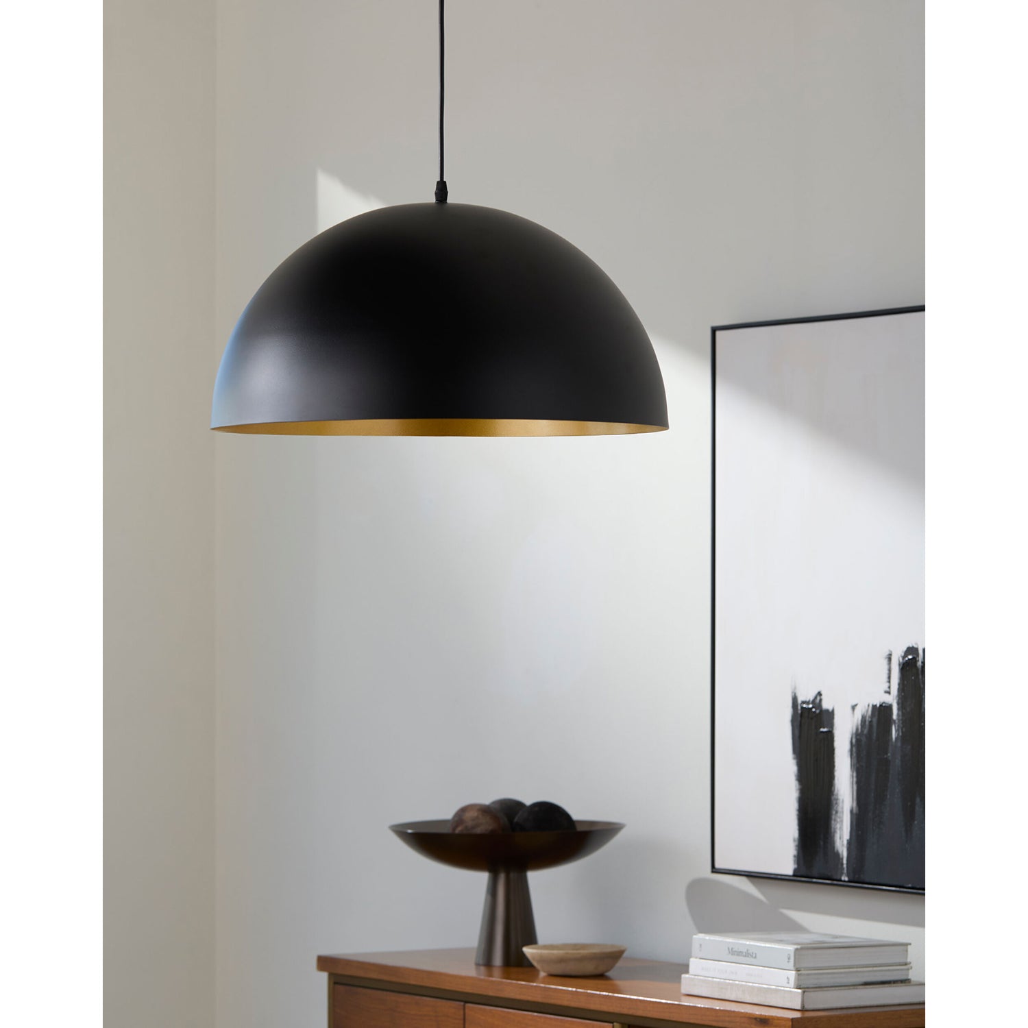 Black pendant light hanging in a room with a abstract painting and decor items on a shelf.