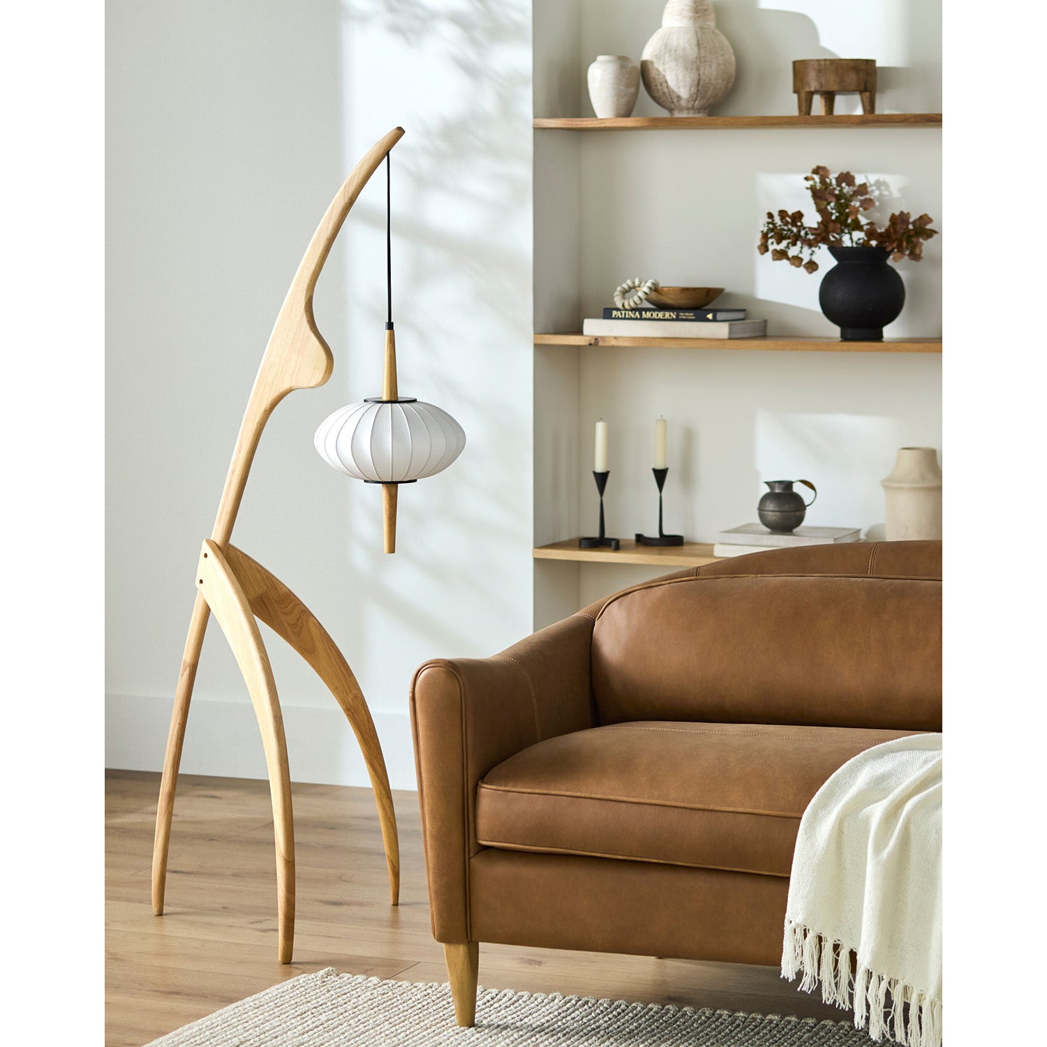 Modern living room with a brown leather sofa, wooden floor lamp, and shelves with decorative items.