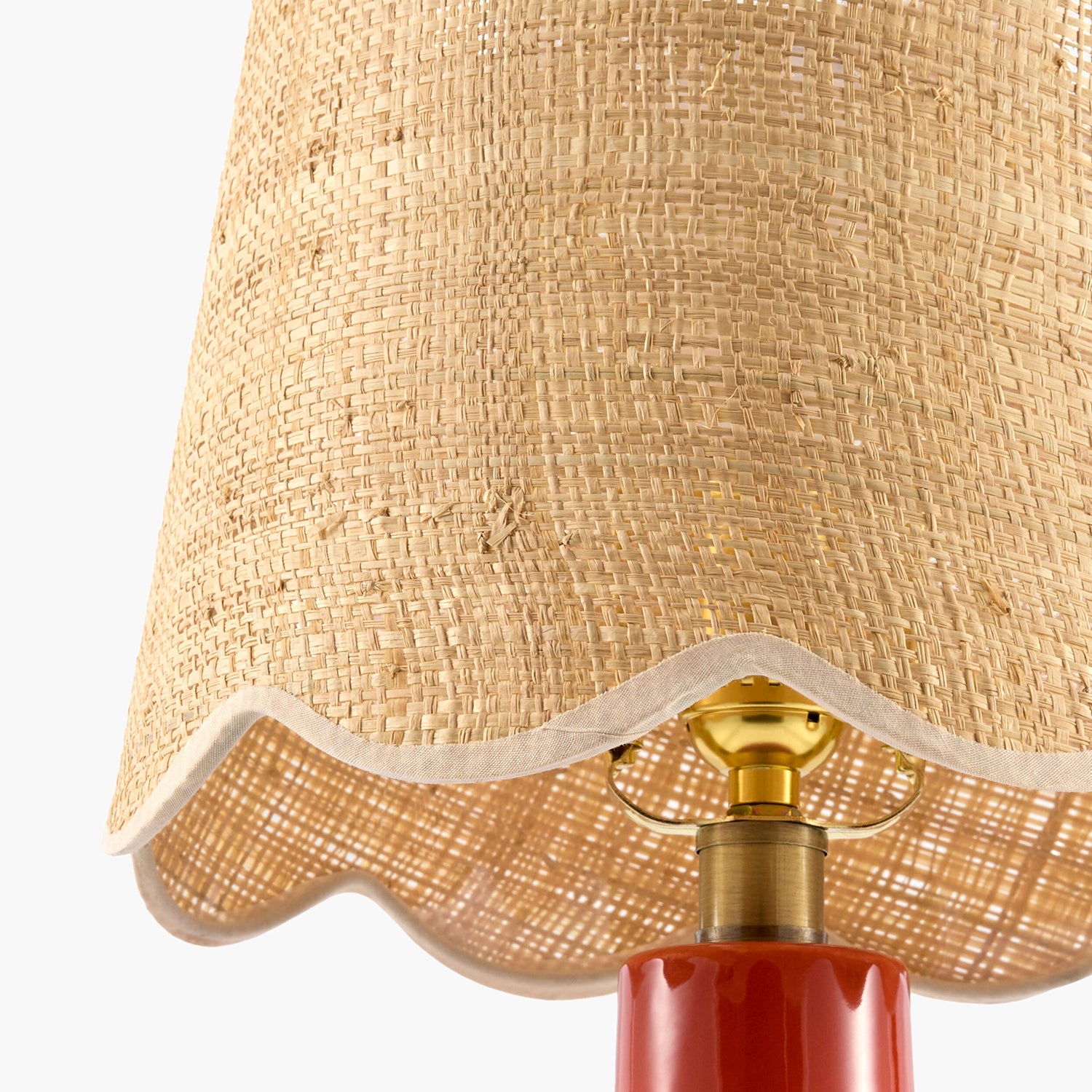 Close-up of a lamp with a beige woven shade and red base.
