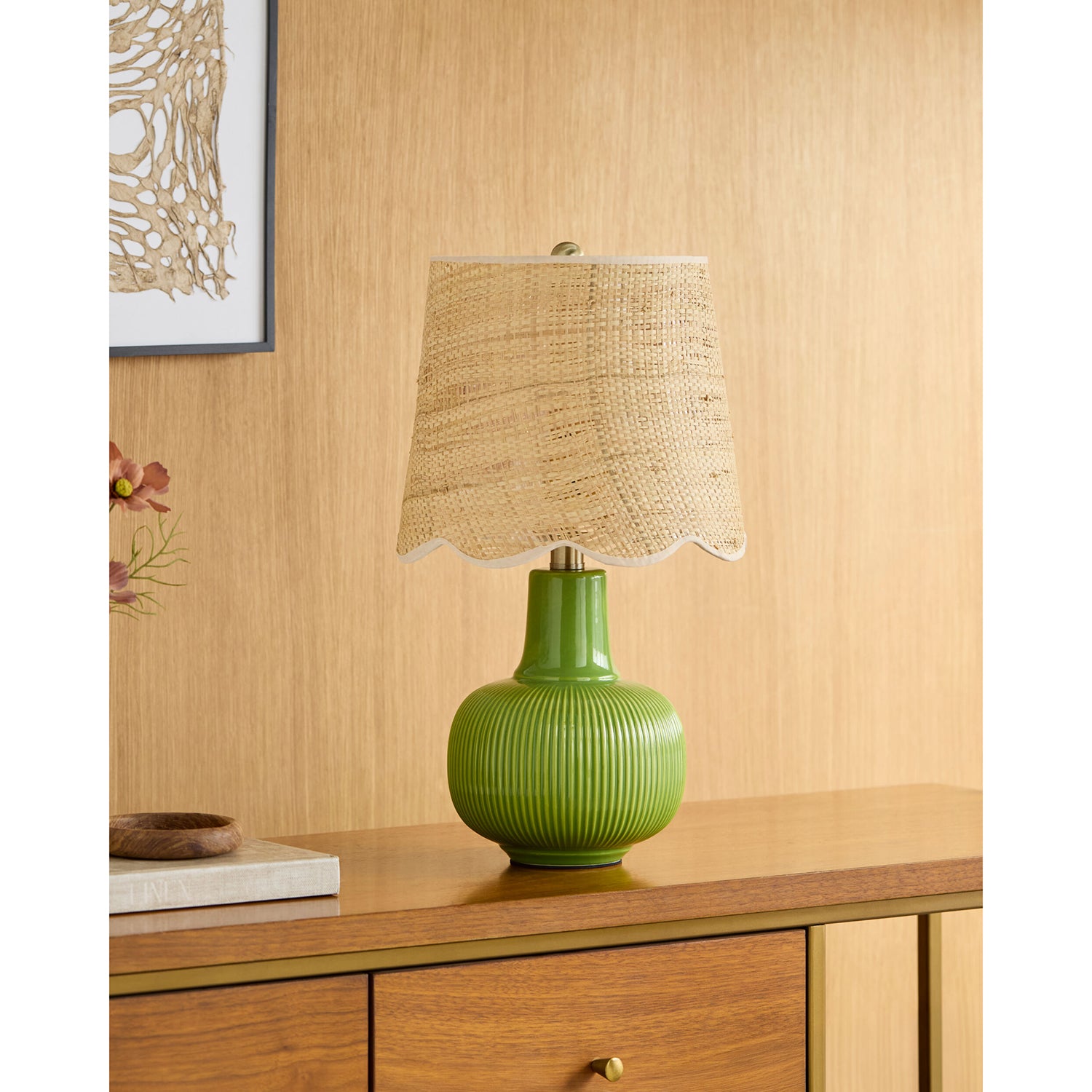 Green table lamp with a beige woven shade on a wooden surface.