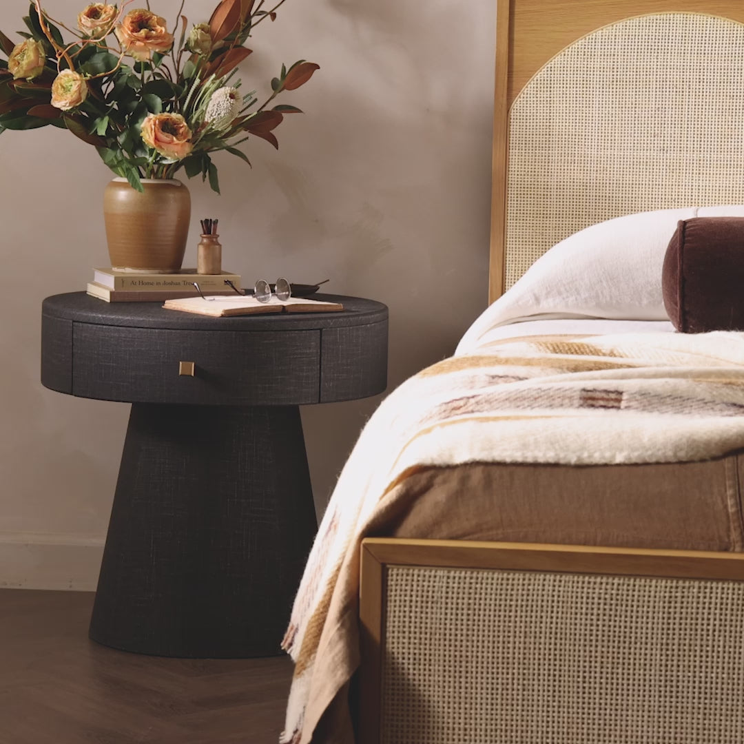 Floral arrangement in a brown vase on a black painted linen round nightstand in a contemporary bedroom 